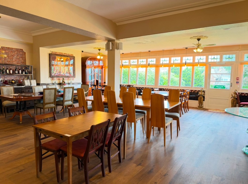 Spacious restaurant dining room with wooden tables, natural light from large windows, and warm decor at The Queens Road Hotel