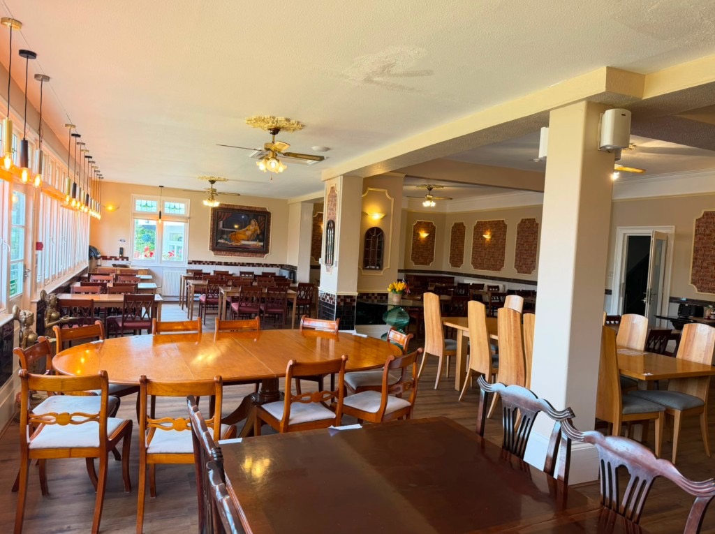 Restaurant dining room with wooden tables, pendant lighting, and large windows at The Queens Road Hotel